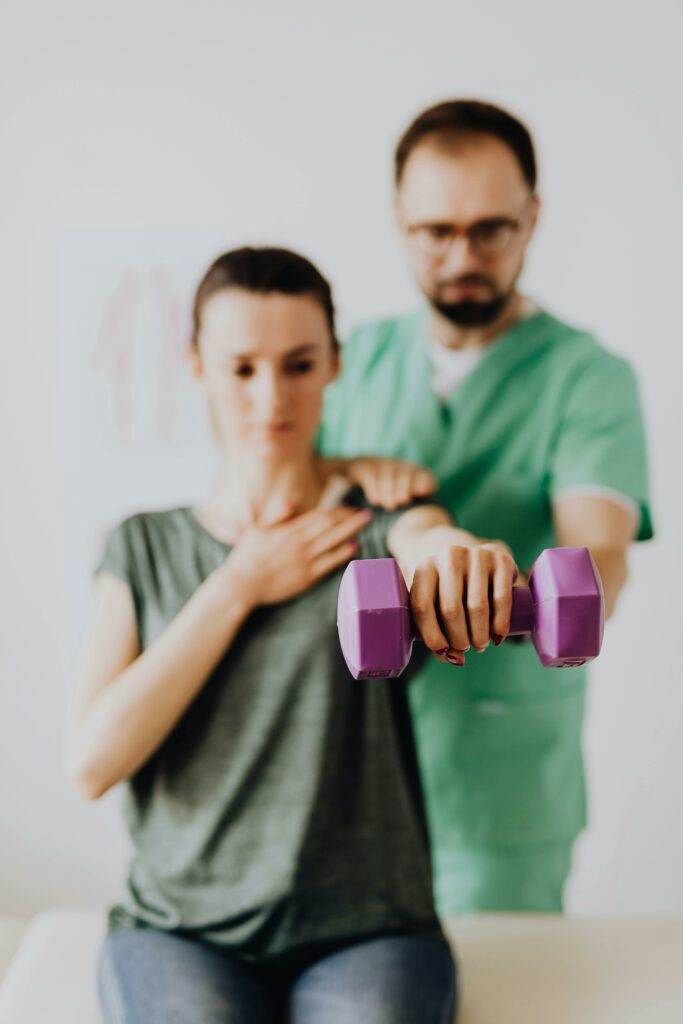 Chiropractor assisting female patient with dumbbell in doctor office