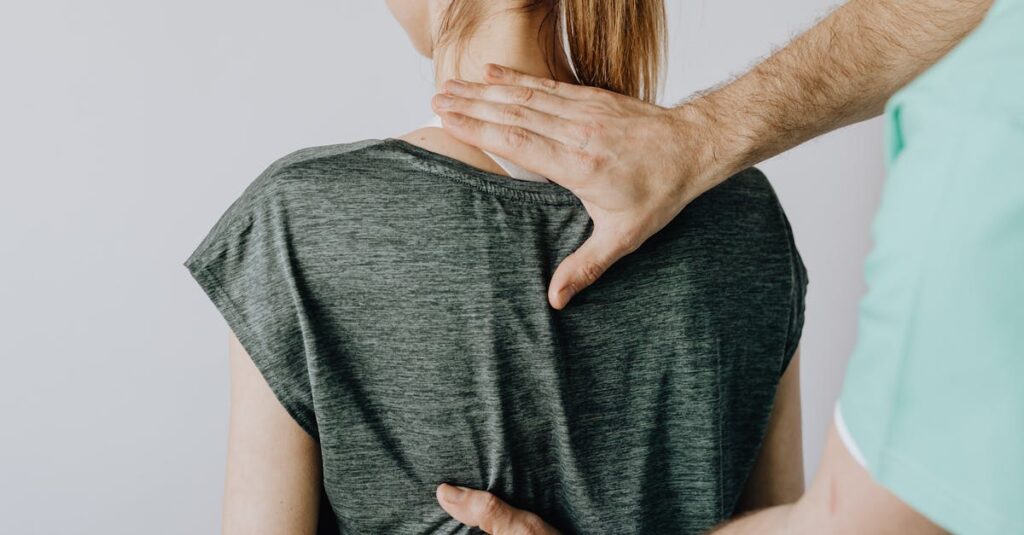 Crop osteopath examining back of anonymous woman in doctor office